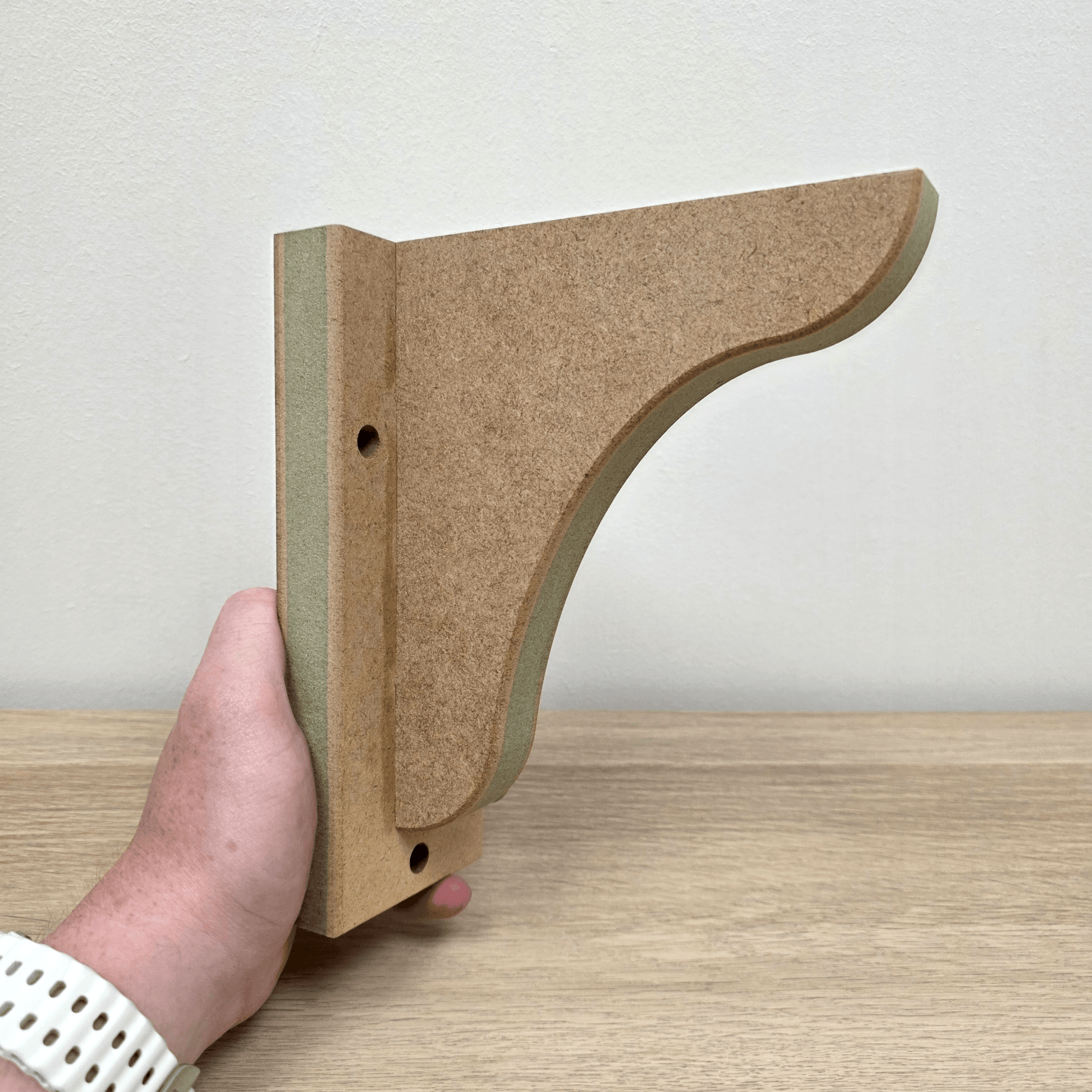 Hand holding a Shaker Gallows Bracket with Backplate - Style 2 on a wooden surface.